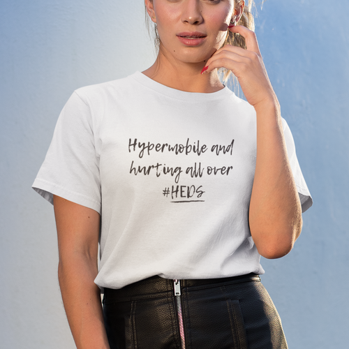 Woman wearing a white t-shirt with text 'Hypermobile and hurting all over #HEDS' and a black leather skirt against a light blue background