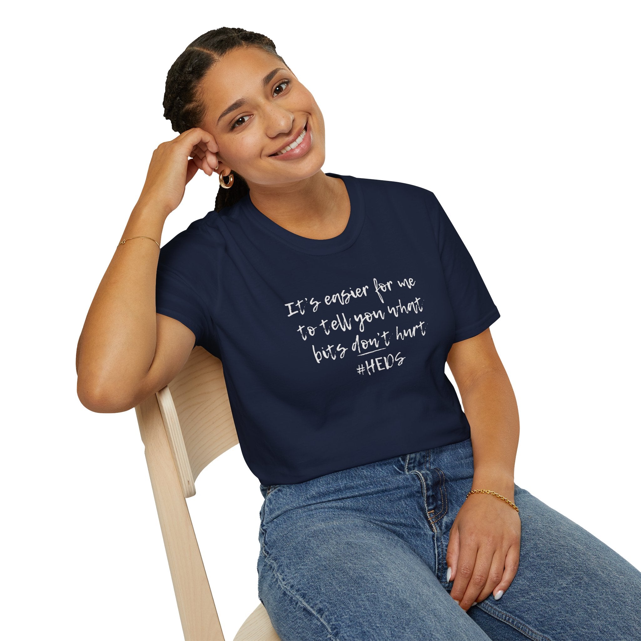 woman sat on chair wearing Navy Softstyle t-shirt with the slogan "It Is Easier To Tell You What Bits Don't Hurt" in bold black text. 